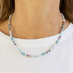 Multicolored bead necklace in blues, greys and whites on a woman with a white Tshirt.