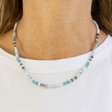 Multicolored bead necklace in blues, greys and whites on a woman with a white Tshirt.