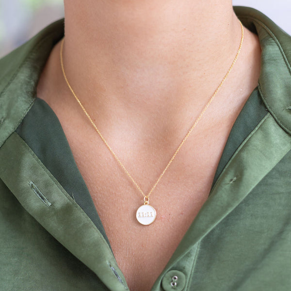 Woman wearing a thin gold necklace with a white circle medallion that says "11:11" on it 