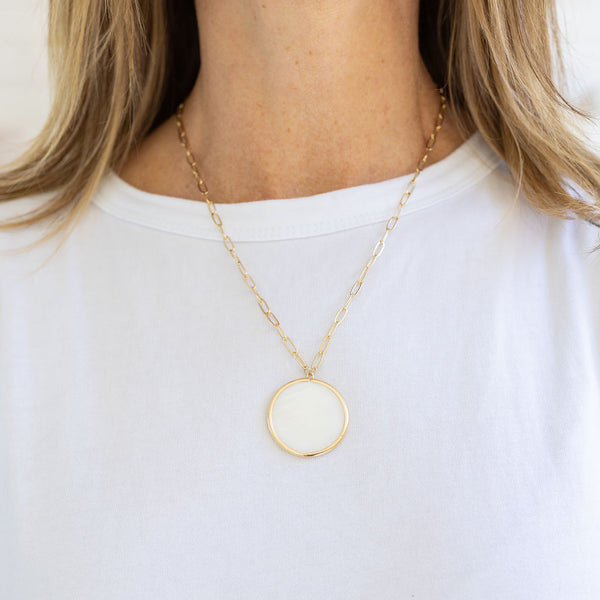 Picture of a gold link chain with a large white disc pendant.