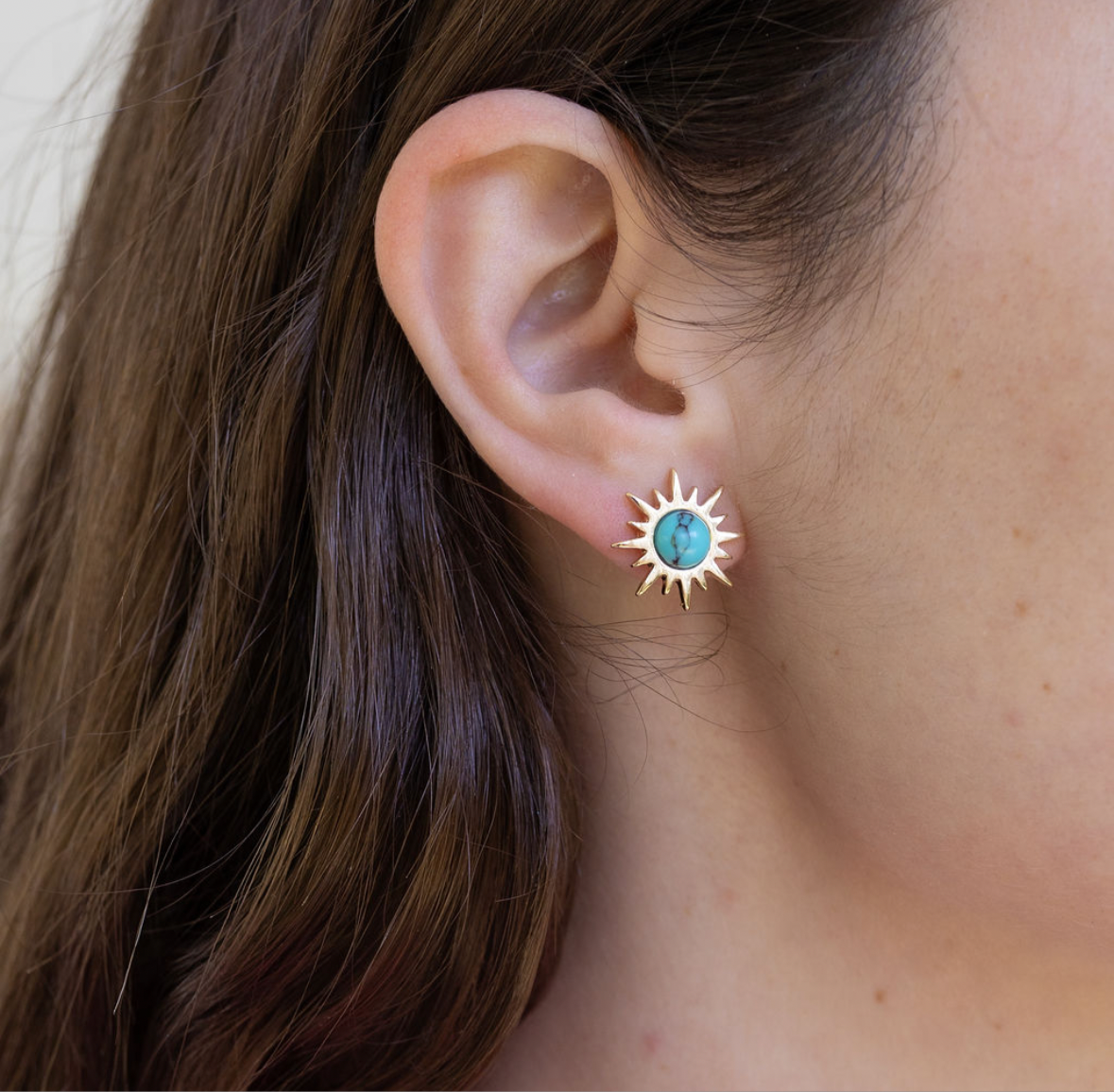 Close-up of an ear wearing a turquoise and gold sun-shaped earring.