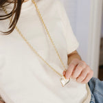 Picture of a woman wearing a long gold chain necklace with a large gold Puffy heart necklace.