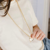 Picture of a woman wearing a long gold chain necklace with a large gold Puffy heart necklace.