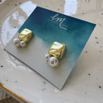 Picture of a pair of gold square studs with two pearls of varying sizes attached to the base of them.
