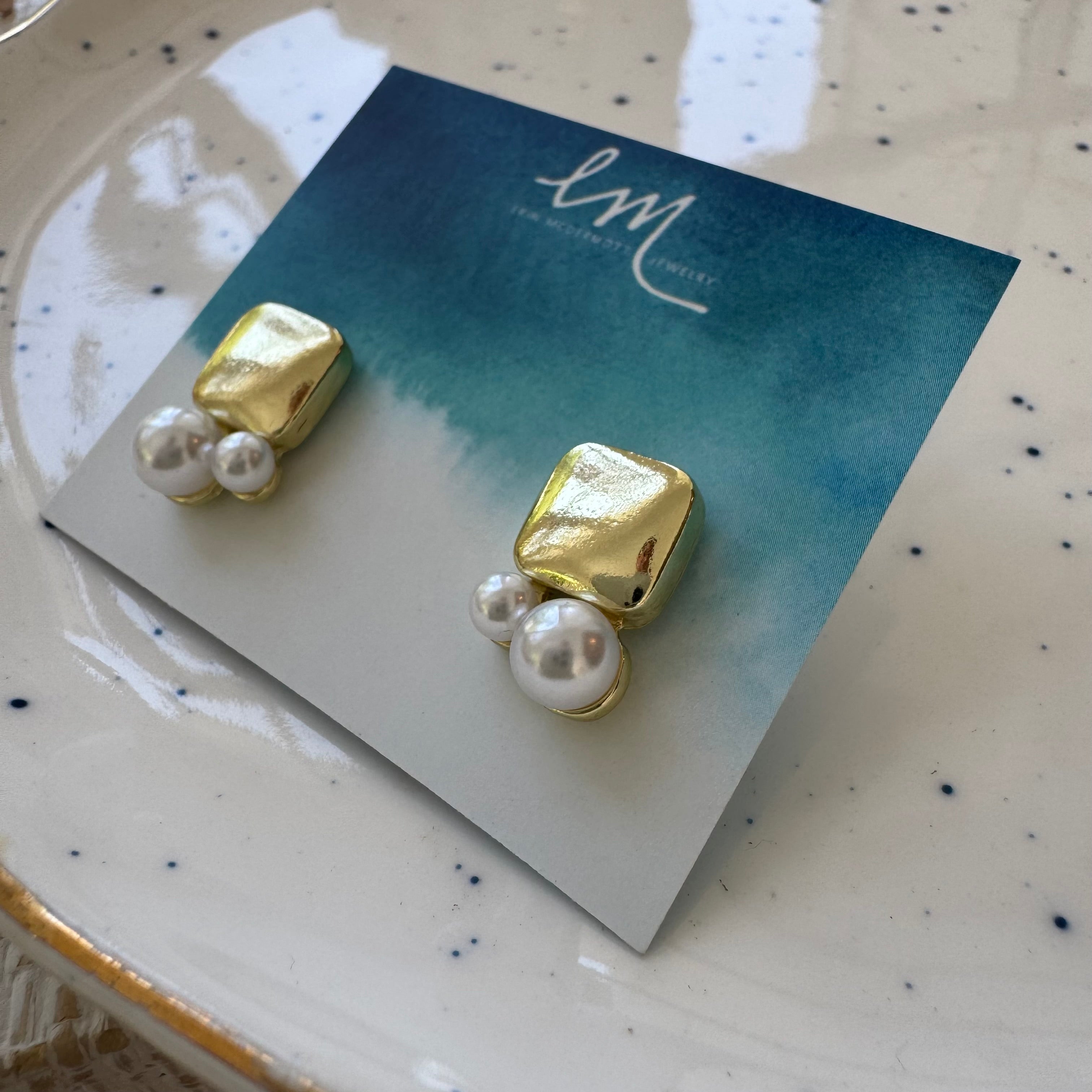 Picture of a pair of gold square studs with two pearls of varying sizes attached to the base of them.