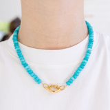 Turquoise beaded necklace with a gold clasp worn by a person on a white background