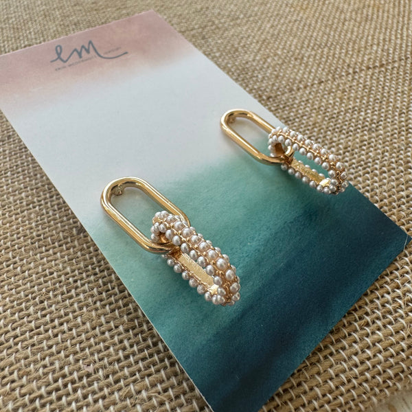 Picture of gold link chain earrings with bottom link encrusted with pearls. Earrings are set in pink and teal ombre earring holder.