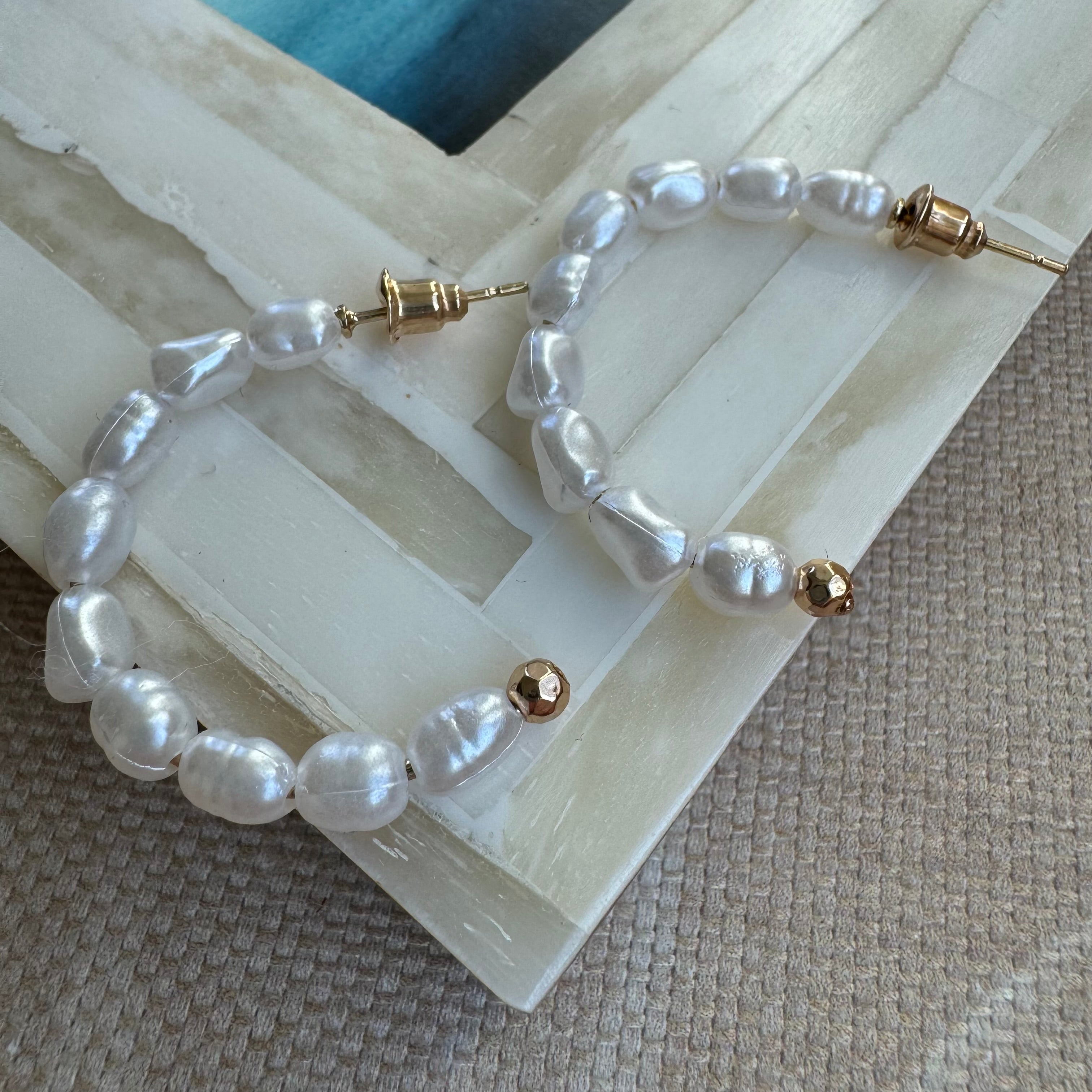 A pair of freshwater pearl hoop earrings laid on a flat surface with natural lighting highlighting the lustrous pearls and metallic hoop details.