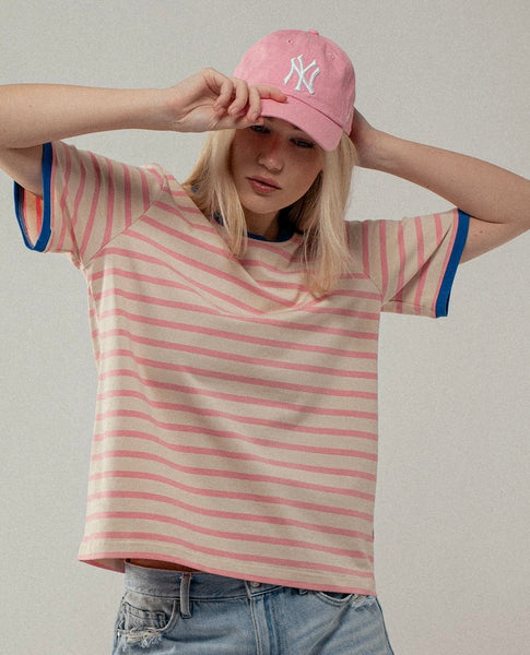 Picture of a model wearing a beige Tshirt with light pink stripes. Tshirt also has blue around the neckline and sleeves.