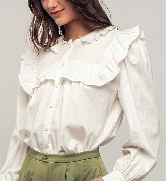 Picture of a model wearing a white long sleeved dress shirt. Shirt has a ruffle collar around the neck and breast and is a button up shirt.