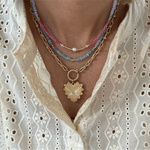 Picture of a stacked set of necklaces. The first necklace is a gold toggle chain necklace with a large heart pendant, second necklace is a delicate blue bead necklace and the third is a pink necklace with a fresh water pearl at it's center.