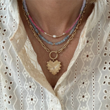 Picture of a stacked set of necklaces. The first necklace is a gold toggle chain necklace with a large heart pendant, second necklace is a delicate blue bead necklace and the third is a pink necklace with a fresh water pearl at it's center.