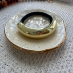 Black hair tie with a Gold ring on a speckled ceramic dish with a textured surface