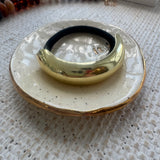 Black hair tie with a Gold ring on a speckled ceramic dish with a textured surface