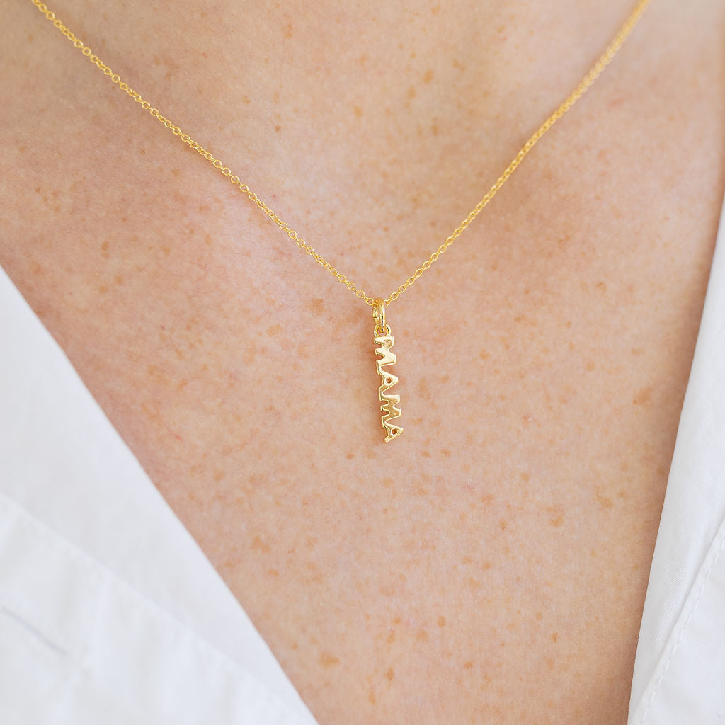 Picture of a woman's neck wearing a a very fine gold chain with a delicate pendant reading "Mama".