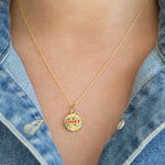 Gold necklace with a 'lucky' pendant worn by a person in a denim jacket.