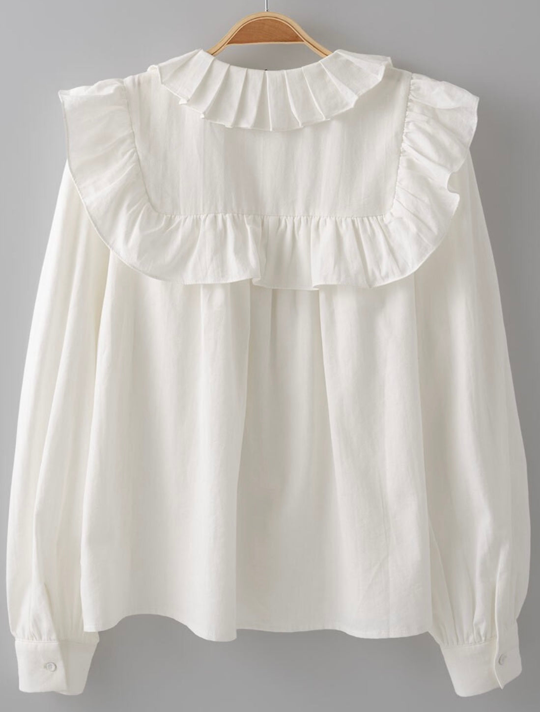 Picture of the back of a white long sleeved dress shirt. Shirt has a ruffle around the collar and the breast and cuff sleeves.