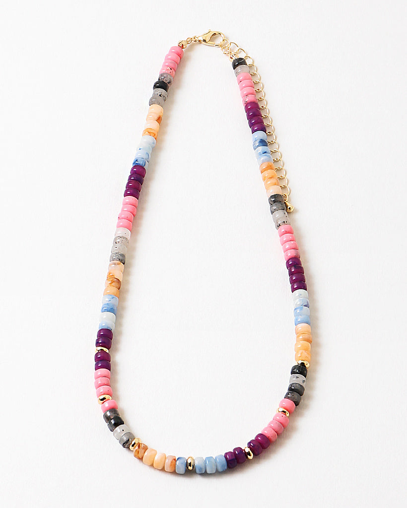 Colorful beaded necklace in pinks, blues, corals and reds with a gold chain and spacers on a white background