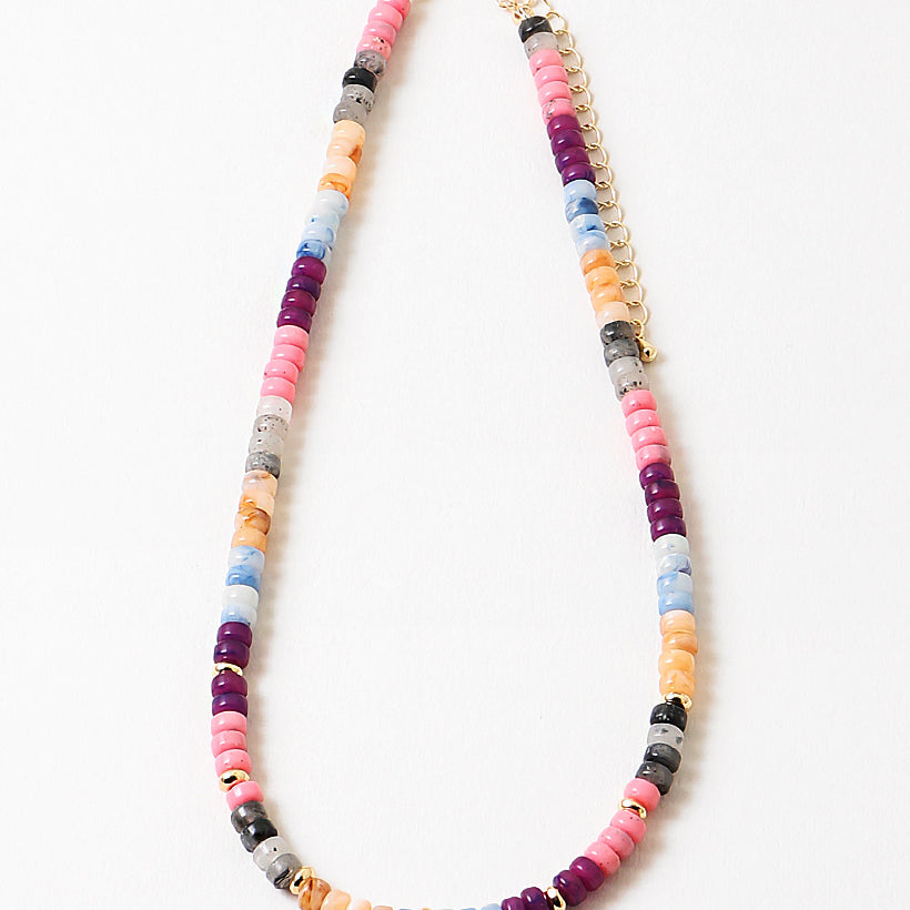 Colorful beaded necklace in pinks, blues, corals and reds with a gold chain and spacers on a white background