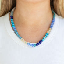 Necklace with blue and green beads worn by a person on a white background