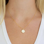Gold necklace with a round pendant with a gold paw print worn by a person
