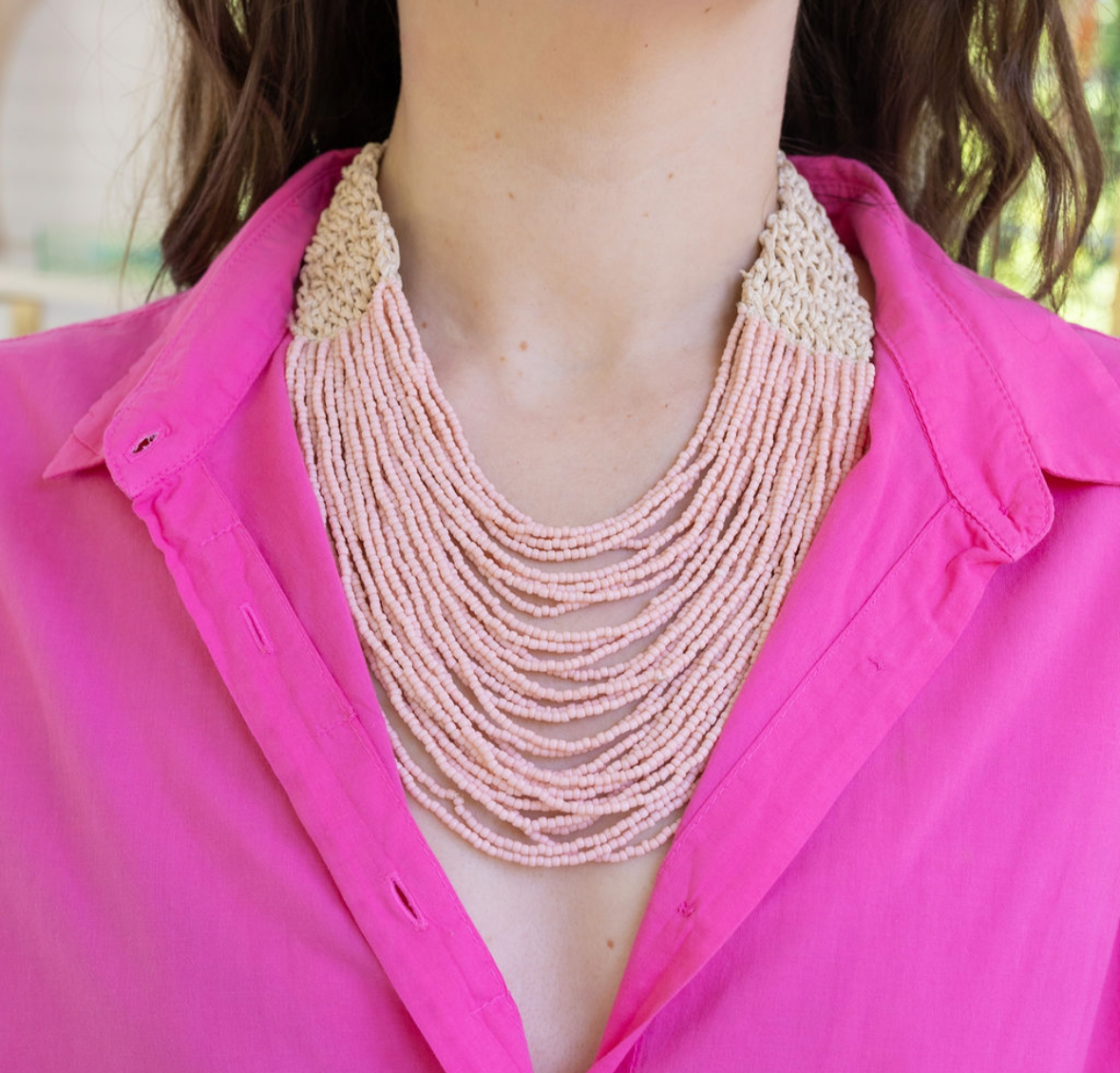Person wearing a multi-strand pink beaded necklace with a pink button up top