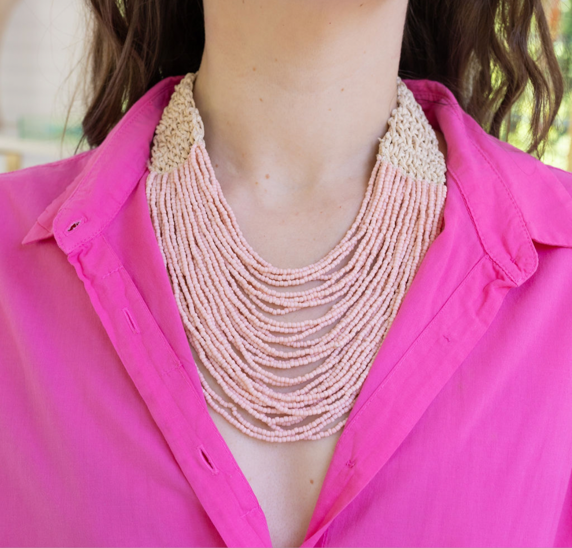 Person wearing a multi-strand pink beaded necklace with a pink button up top