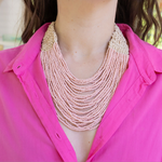 Person wearing a multi-strand pink beaded necklace with a pink button up top