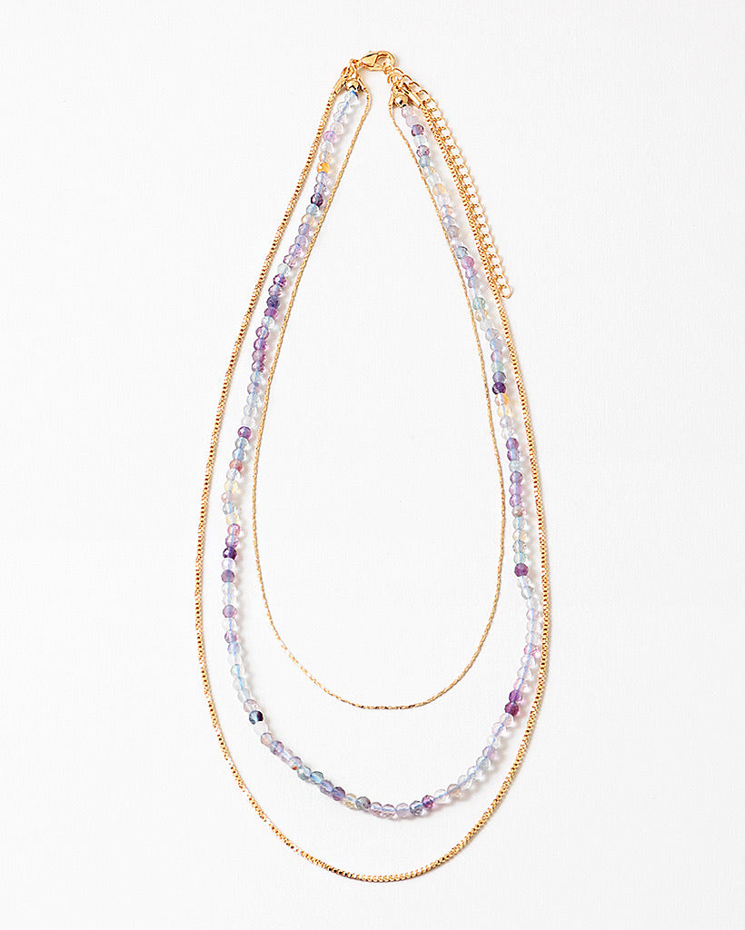 Multistrand beaded necklace with gold chain and clear beads on a white background