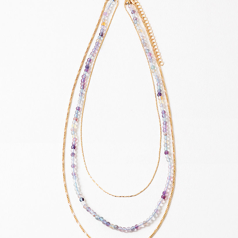 Multistrand beaded necklace with gold chain and clear beads on a white background