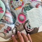 Hand holding open a magazine with a picture of colorful beaded jewelry and a handwritten note with a list outlining what things your need to start your own business.