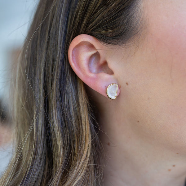 Picture of a woman's ear displaying an opaque white half moon stud outlined in gold.