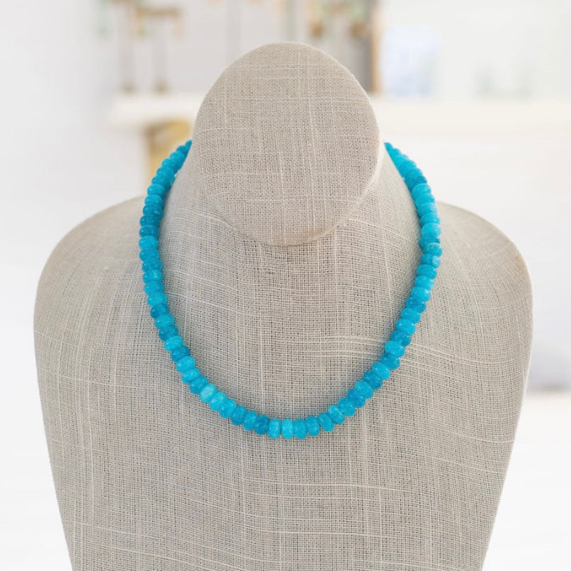 A turquoise gemstone necklace with a gold carabiner clasp, displayed on a mannequin.