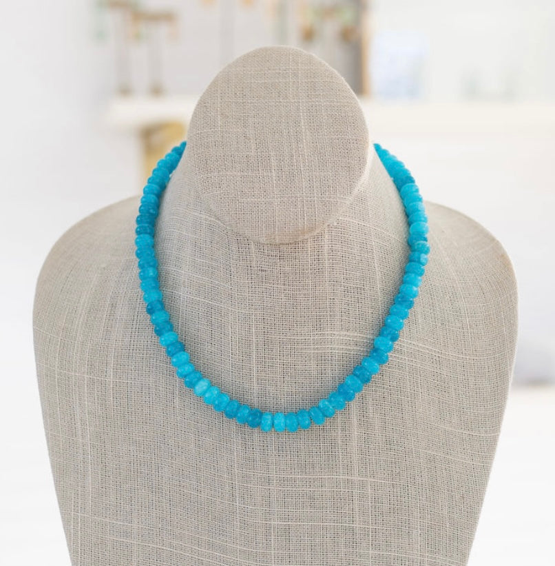 A turquoise gemstone necklace with a gold carabiner clasp, displayed on a mannequin.