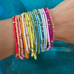 Picture of a wrist wearing 19 different colored seed bead bracelets with accent gold beads.  Bracelets are red, orange, beige, pinks, white, yellows, blues, greens and purple.