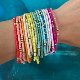 Picture of a wrist wearing 19 different colored seed bead bracelets with accent gold beads.  Bracelets are red, orange, beige, pinks, white, yellows, blues, greens and purple.