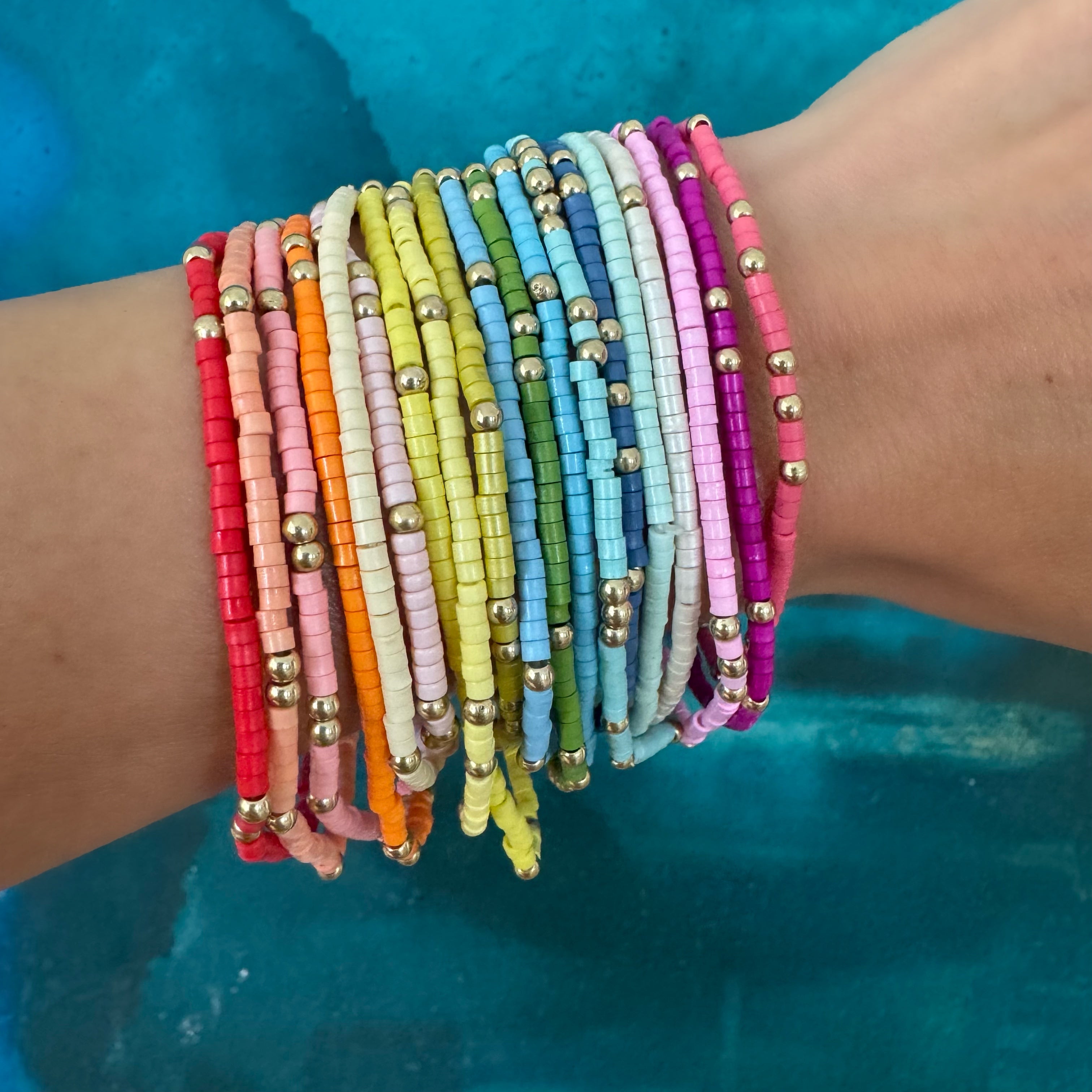 Picture of a wrist wearing 19 different colored seed bead bracelets with accent gold beads.  Bracelets are red, orange, beige, pinks, white, yellows, blues, greens and purple.