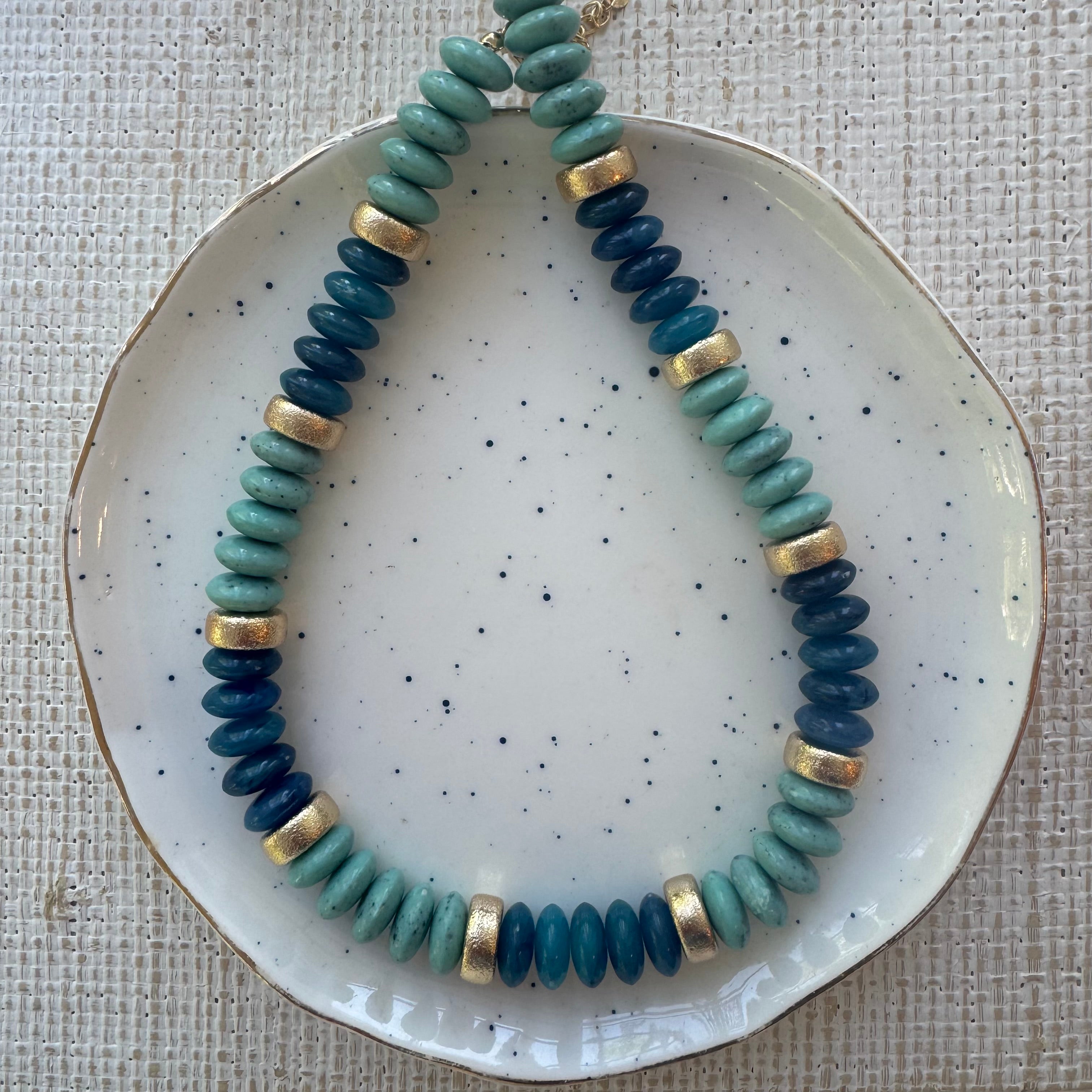 Picture of a resin bead necklace in ombre blues and gold accent spacer beads.
