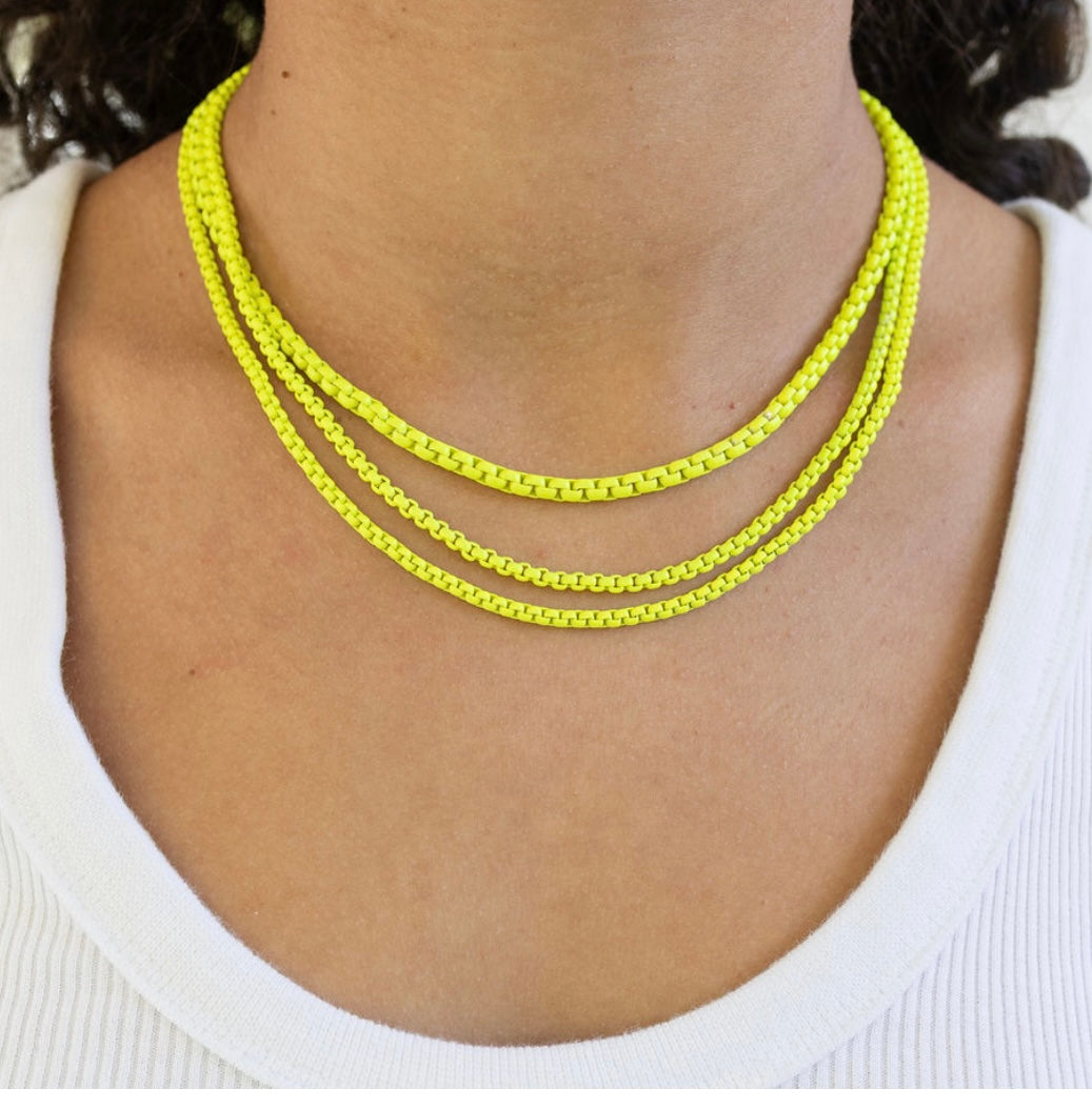 Necklace with three yellow chains on a person wearing a white top.