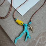 Picture of a woven string necklace with a yellow fish bead, a light blue coral bead, a fresh water pearl and a small gold fish pendant.