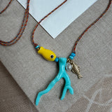 Picture of a woven string necklace with a yellow fish bead, a light blue coral bead, a fresh water pearl and a small gold fish pendant.