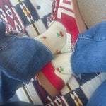 Picture of someone sitting cross legged wearing raw hem jeans, red tennis shoes and white lace socks with small cherries on them.