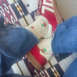 Picture of someone sitting cross legged wearing raw hem jeans, red tennis shoes and white lace socks with small cherries on them.