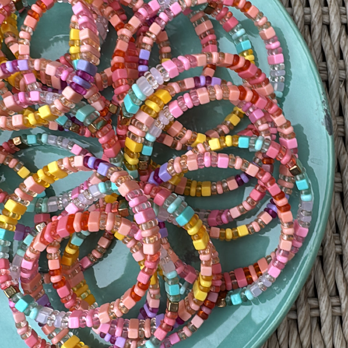 Picture of a blue plate filled with the same bracelet. The bracelet displayed is a multicolored beaded bracelet made up of matte and clear yellow, coral and turquoise beads.