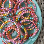 Picture of a blue plate filled with the same bracelet. The bracelet displayed is a multicolored beaded bracelet made up of matte and clear yellow, coral and turquoise beads.