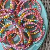 Picture of a blue plate filled with the same bracelet. The bracelet displayed is a multicolored beaded bracelet made up of matte and clear yellow, coral and turquoise beads.