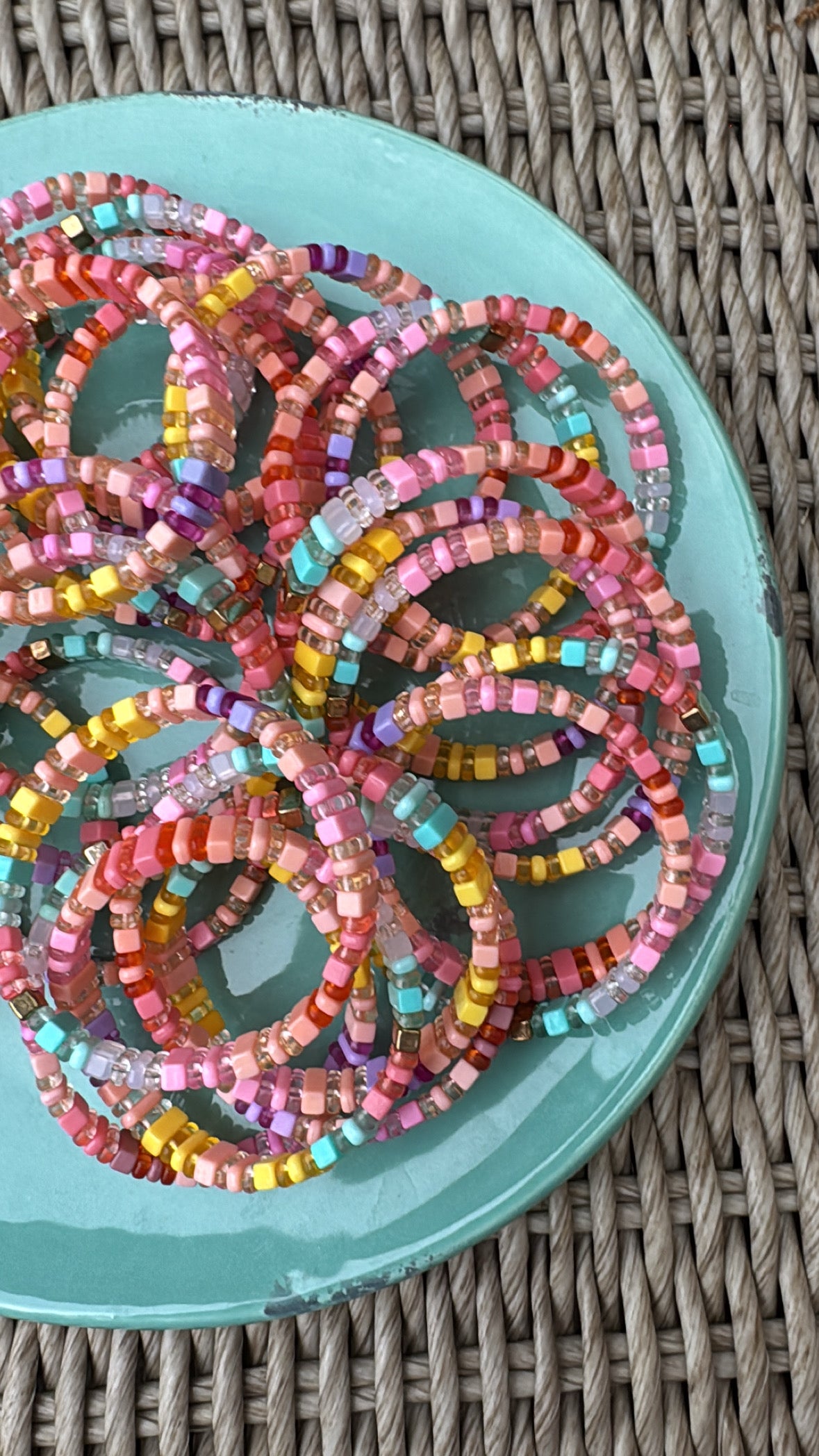Picture of a blue plate filled with the same bracelet. The bracelet displayed is a multicolored beaded bracelet made up of matte and clear yellow, coral and turquoise beads.