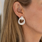 A close-up image of a person wearing silver double loop hoop earrings.
