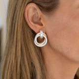 A close-up image of a person wearing silver double loop hoop earrings.