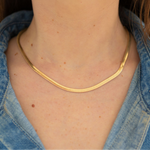 Gold herringbone chain necklace on a person wearing a button up denim shirt